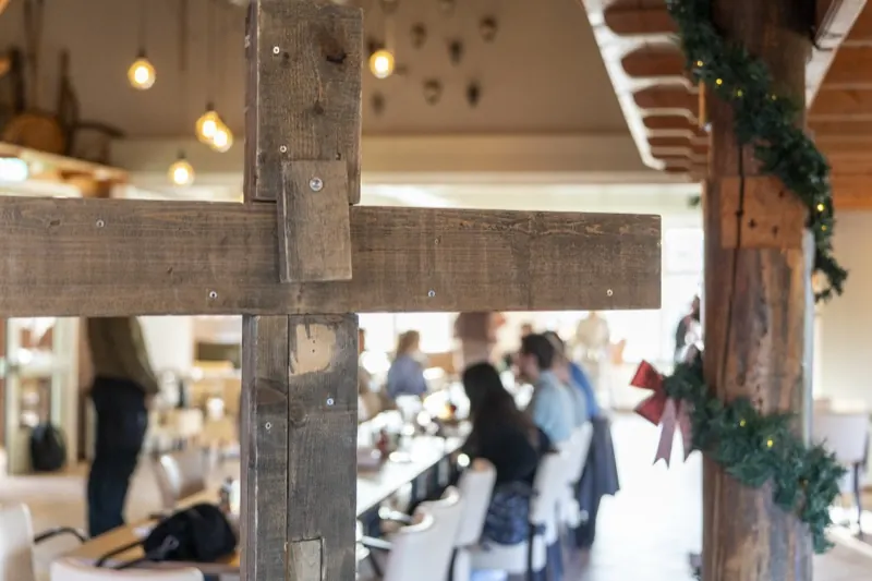 Houten kruis in de zaal, met mensen aan tafel op de achtergrond